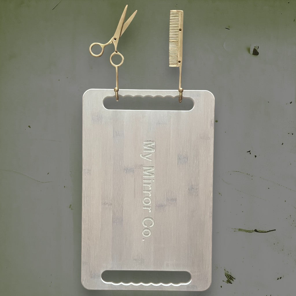 The stylish brass golden scissor and comb duo holding our eco-friendly bamboo mirror in vanilla.